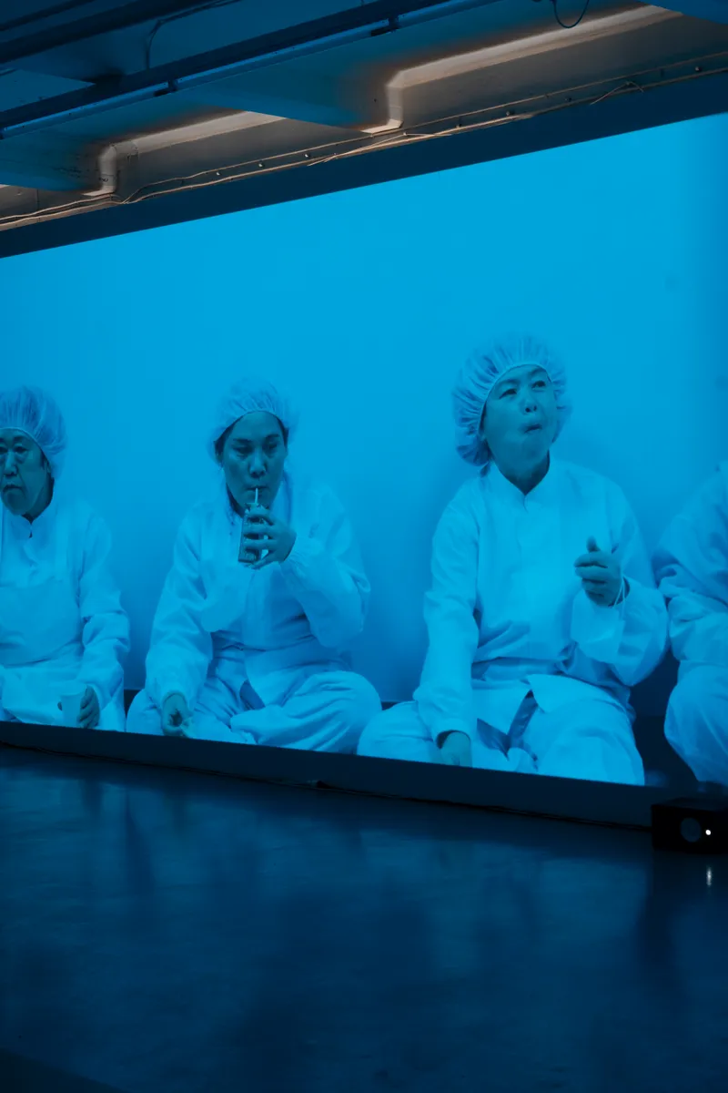 Close view of the projection: women in white hair nets sitting against a wall