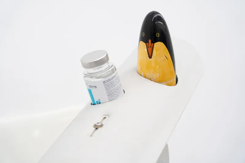 A glass medicine vial and a painted penguin figure set into slots in a curved white surface