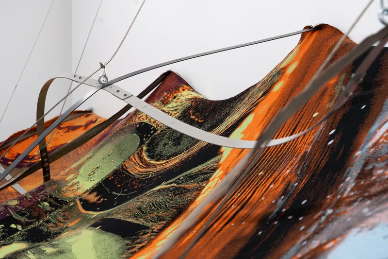 Detail of the printed textile, folds of orange and green held by a metal strap