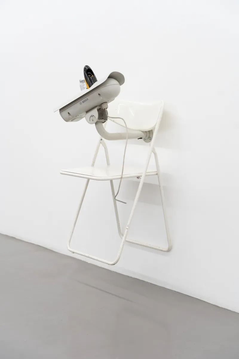 A surveillance camera mounted on a white folding chair fixed to the wall
