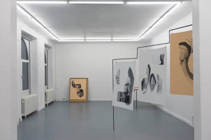 A white gallery with prints of sculpture fragments hung from steel frames and a framed print leaning against the far wall