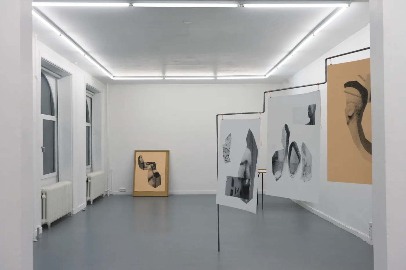A white gallery with prints of sculpture fragments hung from steel frames and a framed print leaning against the far wall
