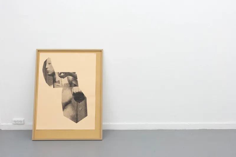 A framed print of fragments of a sculpted head and torso leaning against a white wall