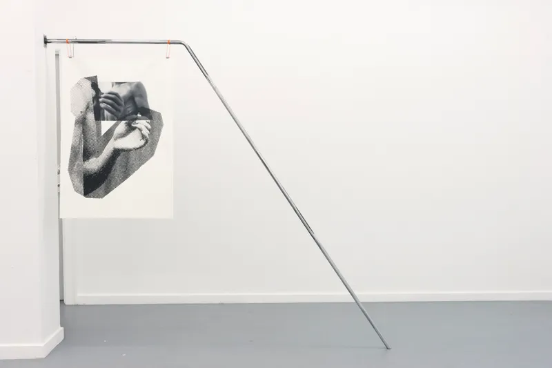 A print hanging from a bent steel tube that leans against the wall