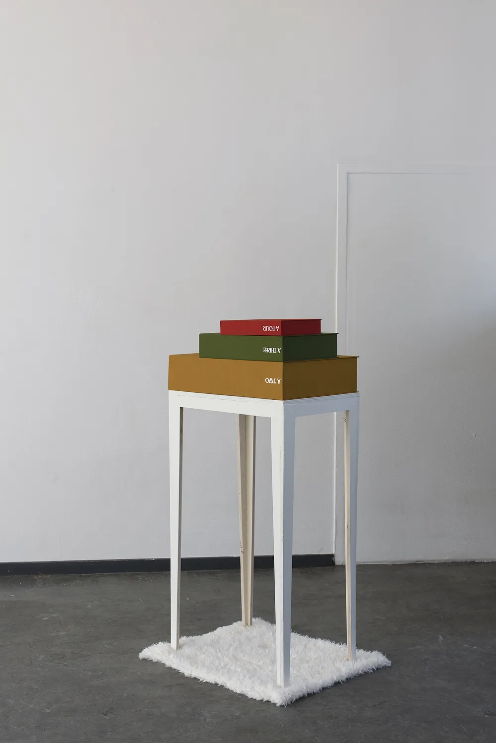 A white plinth with stacked cloth-bound boxes, a red box on top