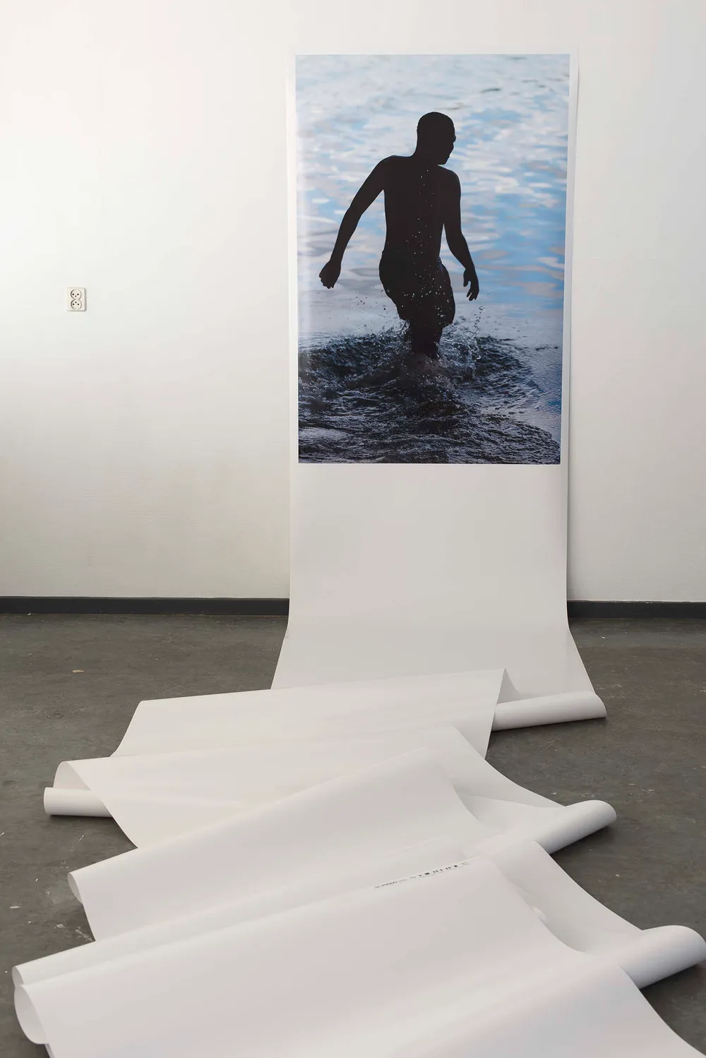 A large print of a swimmer in dark water, a white paper scroll running from it across the floor
