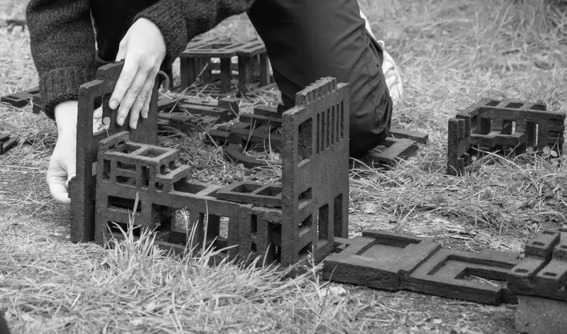 Black and white photo of hands setting up dark cast objects on grass