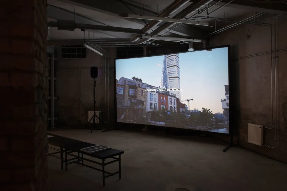 The film projected on a large screen in a concrete basement, a bench with scripts in front