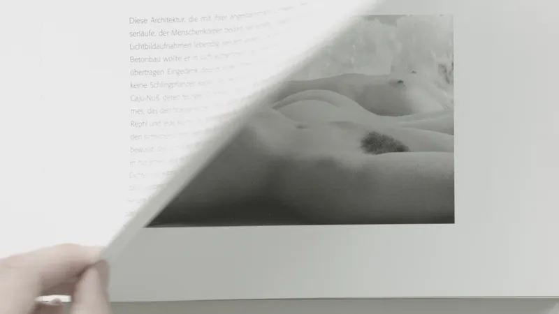 A hand turns the page of a book to a black and white photograph of a reclining nude