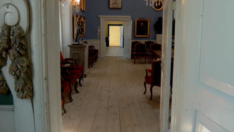 A long hall with portraits, busts and an open door at the end