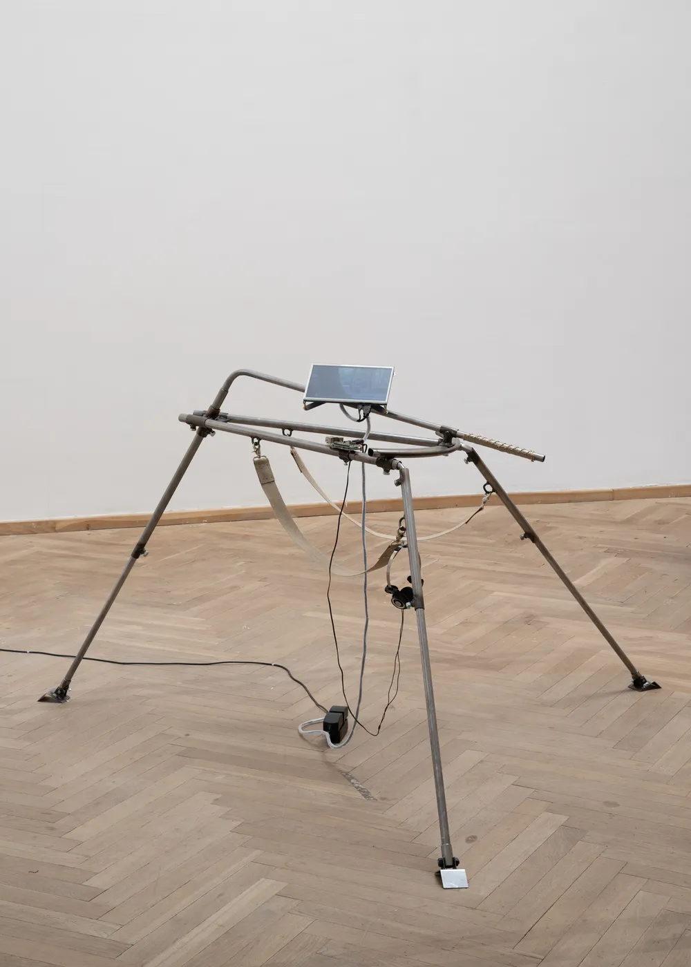 A single steel tripod holding a small screen, cables running to the floor