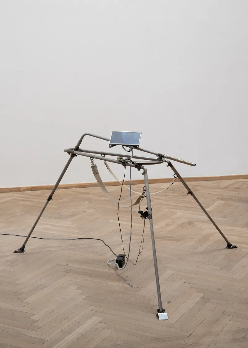 A single steel tripod holding a small screen, cables running to the floor