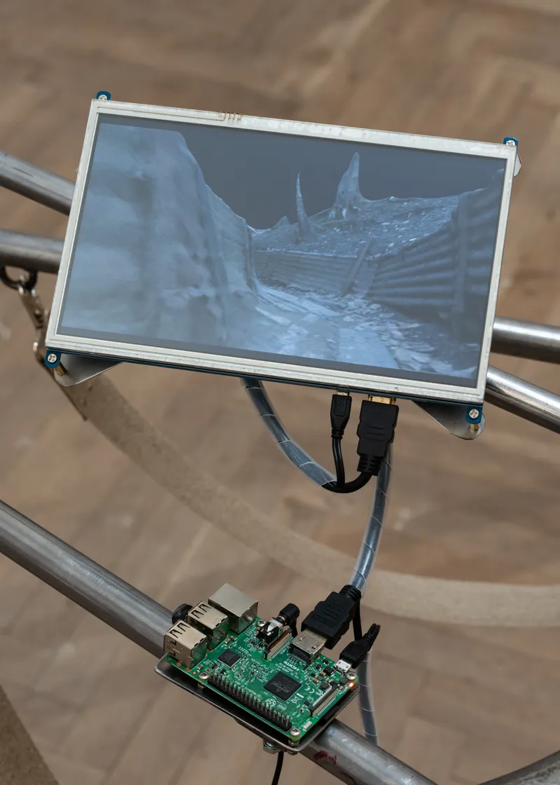 Close-up of a small screen showing a grey trench, mounted on a steel tube with a circuit board